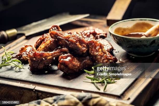 baked chicken wings with sesame seeds and sweet chili sauce on wooden cutting board. barbecue chicken wings close up on wooden tray. - poultry netting stock pictures, royalty-free photos & images
