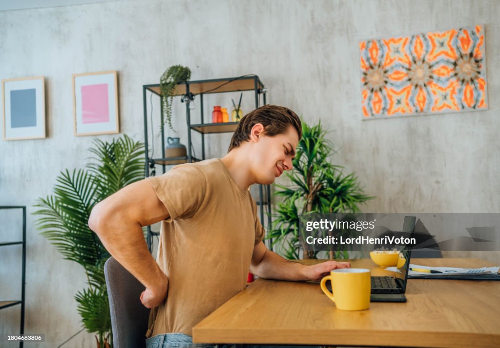 Young man suffering from back pain while working at home