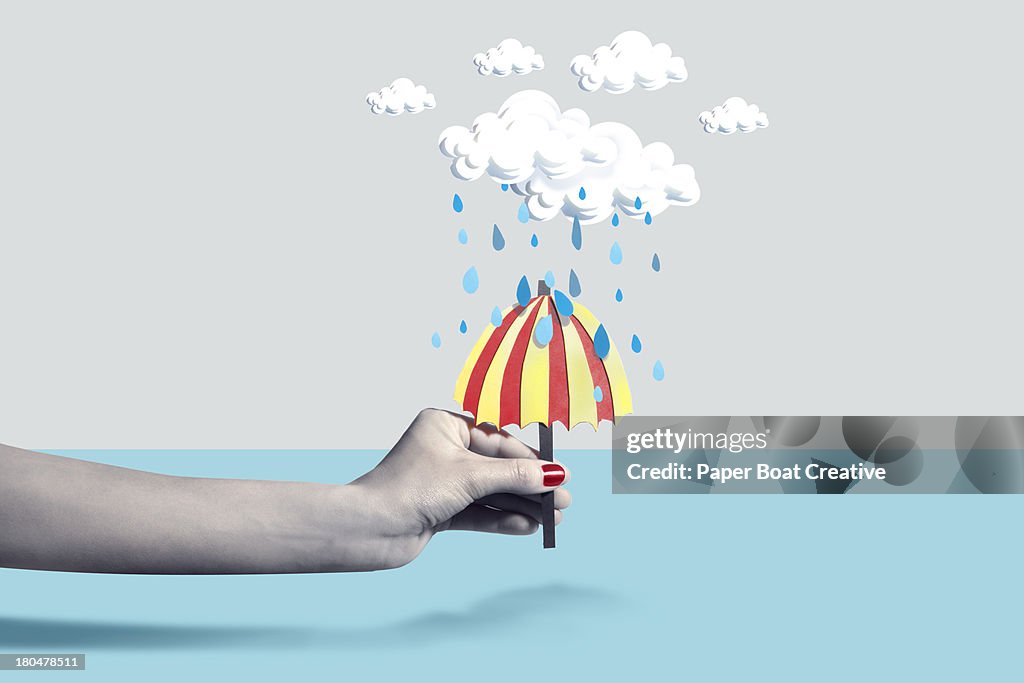 Hand holding paper craft umbrella under rain cloud