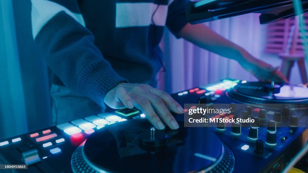 Young Asian woman dj girl playing music and scratching tracks on professional dj midi controller at colorful house party at night. Multicultural friend having fun together college house party.