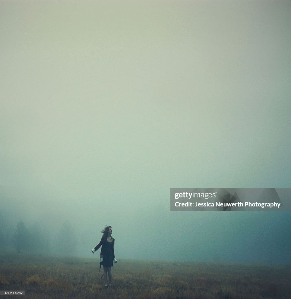 Young woman in sweater standing in misty field