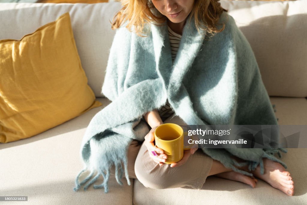 Close-up of woman wrapped in blanket drinking tea in the living room