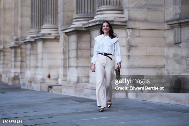 Alba Garavito Torre wears a white large collar and puffy sleeves with bow shirt, ivory high waist wide legs pants from Nina Blanc, brown and white...
