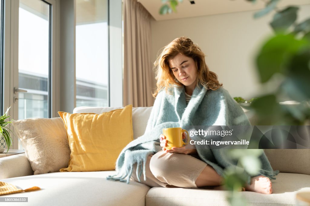Woman wrapped in blanket drinking tea in the living room