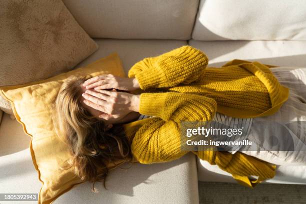 sick oman lying on sofa and covering her eyes with hands - sindrome premestruale foto e immagini stock
