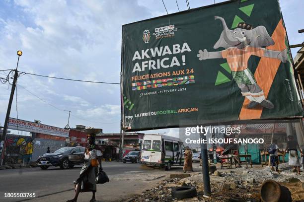 People walks past a billboard of the 2024 Africa Cup of Nations in a street in Abobo, a suburb of Abidjan on November 24, 2023.