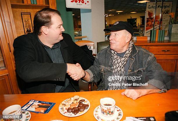 Jürgen Roland, Andreas Ellermann,;Signierstunde, Möbelpark Sachsenwald,;Bentdorf bei Hamburg, Deutschland, Tasse,;Kekse, Gebäck, Tisch, Mütze,