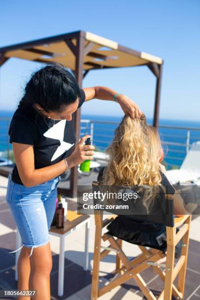 fashion team female hairdresser spraying and ruffling model's hair on the terrace at the seaside - ruffling stock pictures, royalty-free photos & images