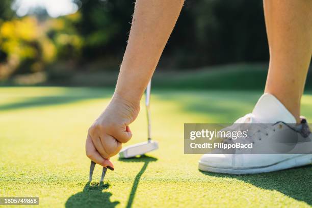 una golfista está elevando la marca del pitch en el green - chuleta fotografías e imágenes de stock