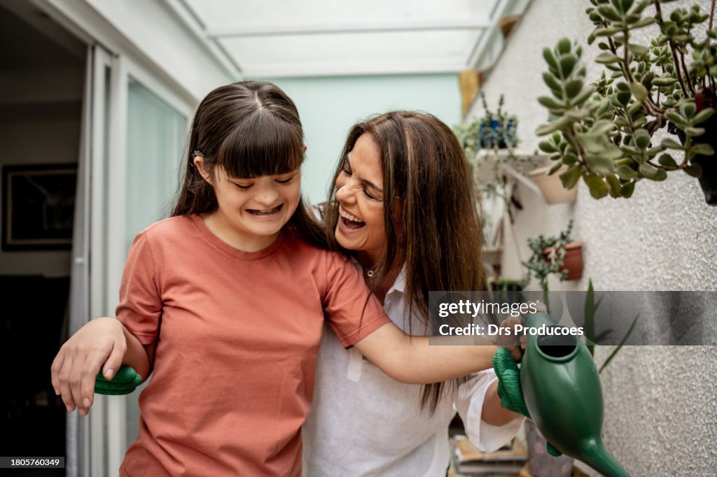 Daughter with down syndrome and mother watering plants in the garden
