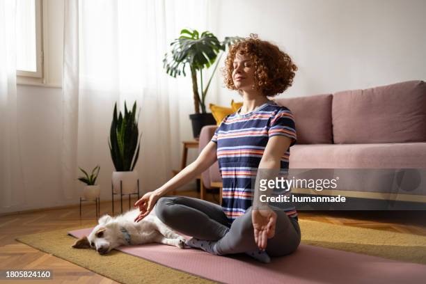 ginger woman meditating in her living room - person meditating stock pictures, royalty-free photos & images