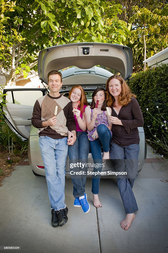 Family of four sharing popsicles on car trunk