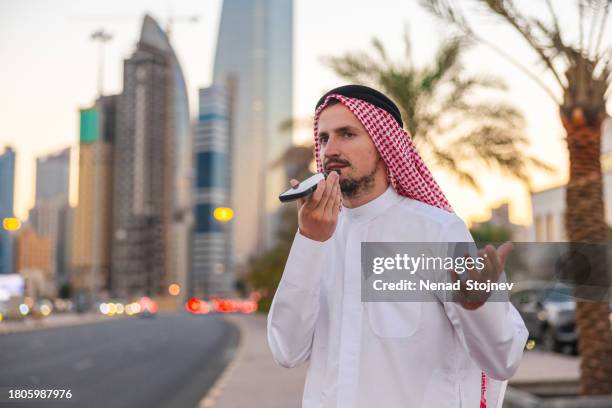 young sheik talking on the phone while walking in the city during sunset - kuwait towers stock pictures, royalty-free photos & images