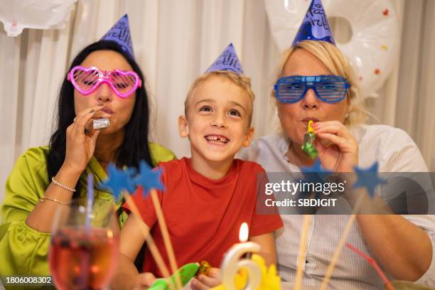 caucasian boy, celebrating his 6th birthday with his mothers, at their home while blowing a party horn blower - party horn blower imagens e fotografias de stock