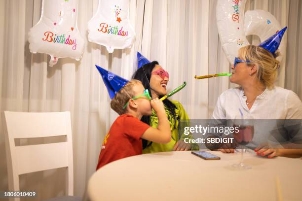 caucasian boy celebrating his birthday while blowing a party horn blower with mother and aunt - party horn blower imagens e fotografias de stock