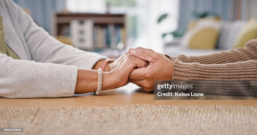 People, holding hands and closeup on table for care love or retirement support, compassion or trust. Couple, partnership and fingers for difficult news or loss comfort, fear solidarity or grief help