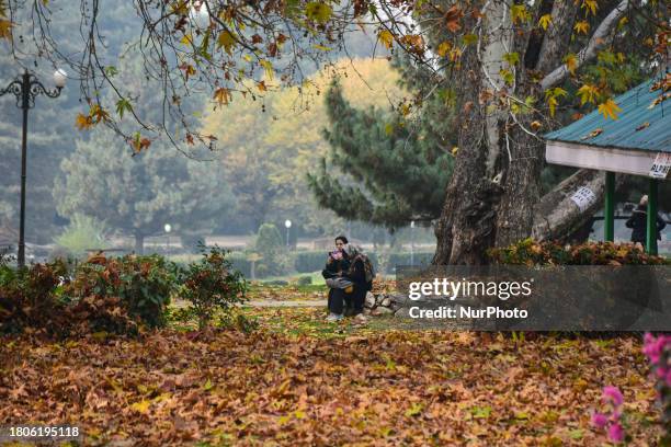 People are resting on a bench during a cold autumn day in Kokernag, south of Srinagar, Indian Administered Kashmir, on November 27, 2023.