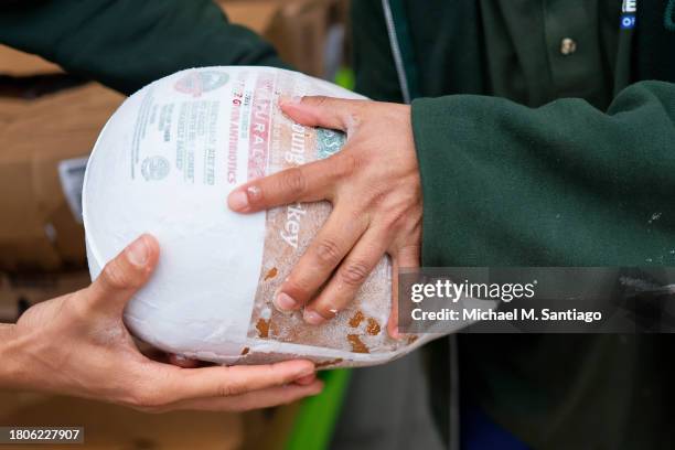 Workers pass a frozen turkey during a giveaway at Green Valley of Sunnyside Market Place on November 21, 2023 in the Sunnyside neighborhood of Queens...