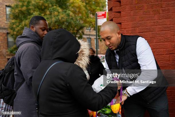 Assemblyman Juan Ardila places a frozen turkey in a bag during a giveaway at Green Valley of Sunnyside Market Place on November 21, 2023 in the...