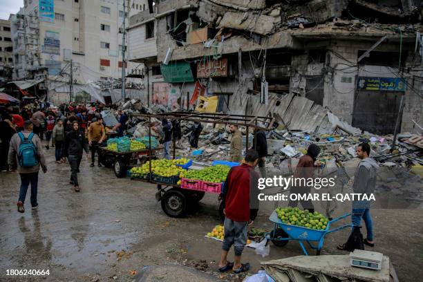 Palestinians sells vegetables in front of a building destroyed in an Israeli strike, near Al-Zawiya market in Gaza City on November 27 on the fourth...