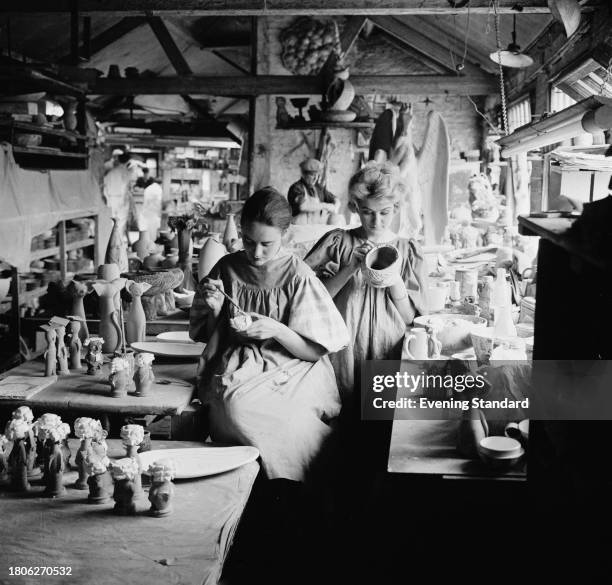 Two women paint objects at the Chelsea Pottery workshop full of figurines and pots, London, June 21st 1961.