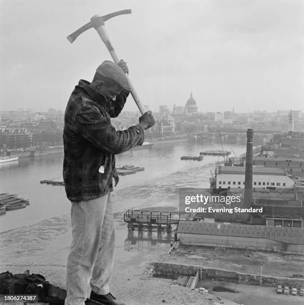 Demolition worker with a raised pickaxe stands on The Shot Tower at the South Bank of the River Thames during its demolition, London, March 26th...