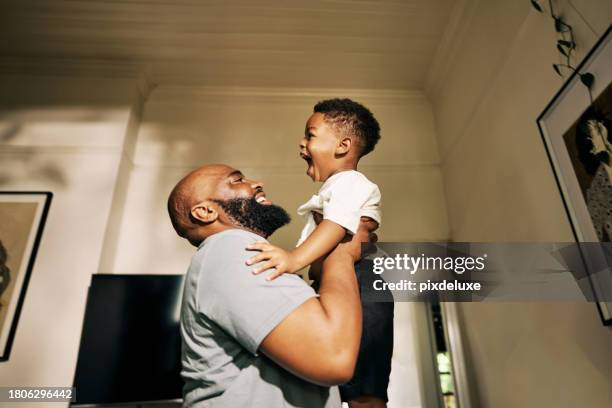 un alegre abrazo mientras un radiante padre levanta a su alegre hijo en lo alto de un pasillo iluminado por el sol de su casa - lifting someone up fotografías e imágenes de stock