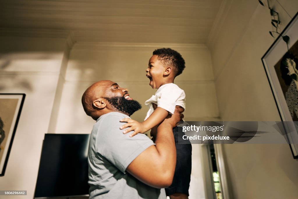 Joyous Embrace as a Beaming Father Lifts His Gleeful Son High in a Sunlit Corridor of Their Home