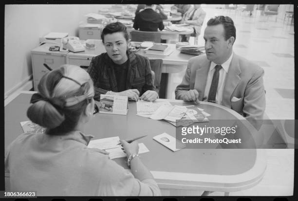 At an American Express office, an agent fills out paperwork for a couple applying for a credit card, Washington DC, October 8, 1958. Various...