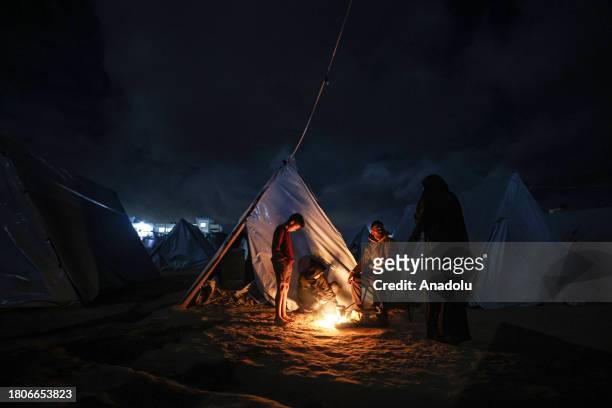 Displaced Palestinians, living in tents, light a fire to keep warm as they struggle with cold weather under limited means and difficult conditions...