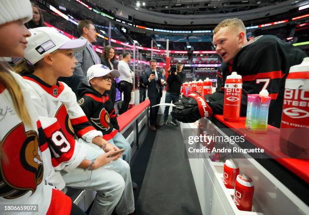 Brady Tkachuk of the Ottawa Senators talks with young fans watching warm-up from the bench on Hockey Fights Cancer night prior to a game against...