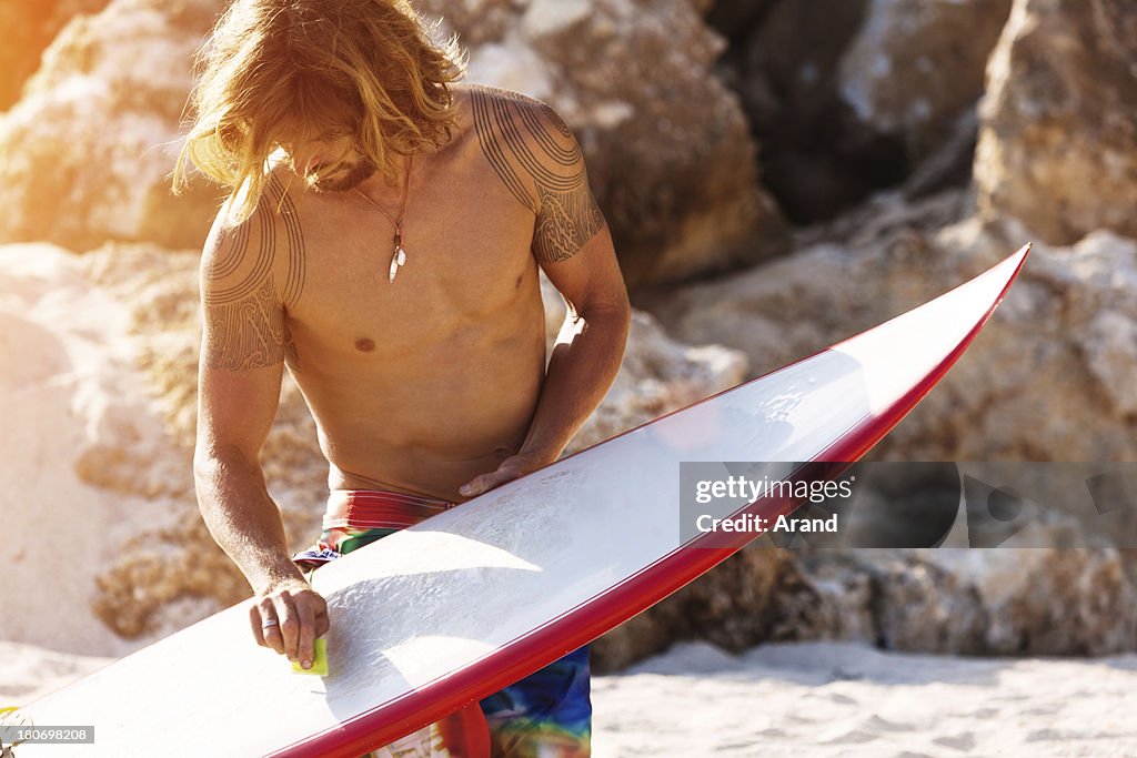 Surfer on a beach waxing surfboard