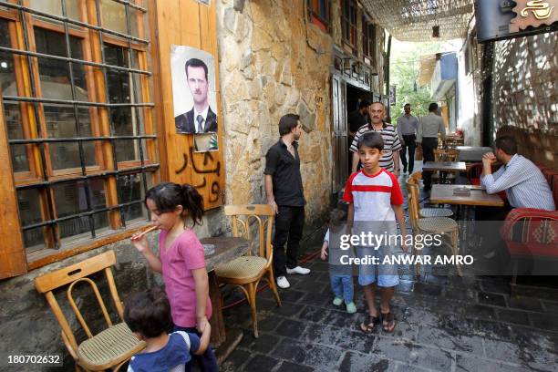 People walk past the terrace of a restaurant neat a poster featuring Syrian President Bashar al-Assad in the capital Damascus on September 16, 2013....