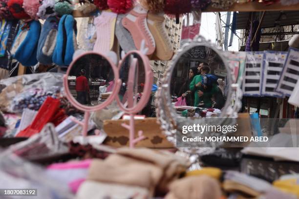 Family is reflected in the mirror on a street vendor's stall in an open-air market in the southern Gaza Strip city of Khan Yunis on November 28,...