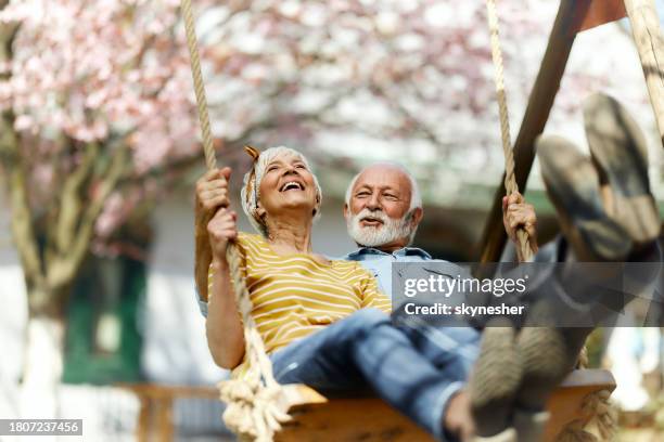 feliz pareja de ancianos columpiándose durante el día de primavera en el patio trasero. - pareja madura fotografías e imágenes de stock