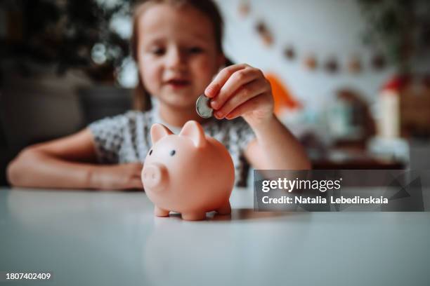 future finance: girl child taking the first steps in financial responsibility, saving in the piggy bank. - money box stock pictures, royalty-free photos & images