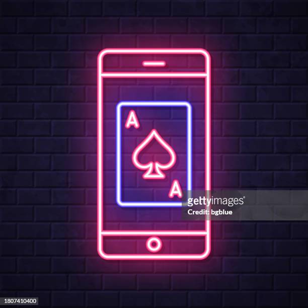 smartphone with playing card. glowing neon icon on brick wall background - blackjack stock illustrations