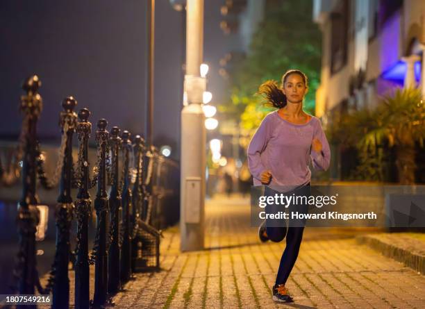 female jogger exercising at night - one mid adult woman only stock pictures, royalty-free photos & images