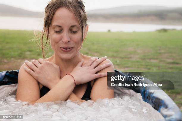 woman inside a iced bath tube inhaling with eyes closed - eis baden stock-fotos und bilder