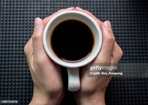 someone hands holding a mug of black coffee before drinking. - koffie stockfoto's en -beelden