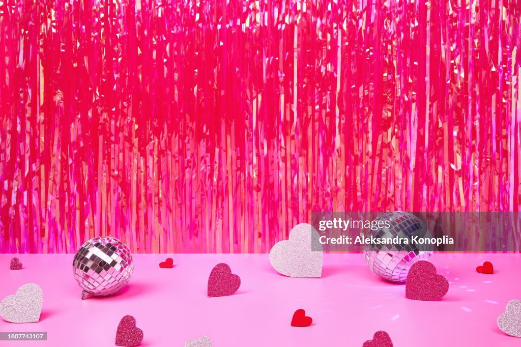 Bright pink Valentine's day background with hearts, shiny disco balls and holographic magenta pink tinsel curtain. Trendy retro 80's, 90's romantic disco party backdrop