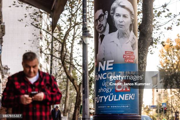 People pass in front of a poster advertising the Hungarian government's national consultation launch on November 22, 2023 in Budapest, Hungary. This...