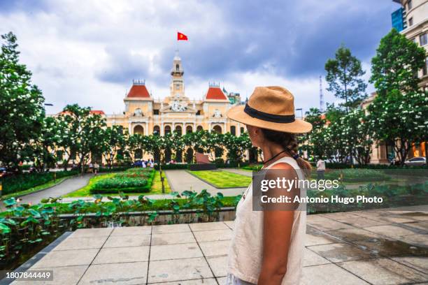 young woman wearing a hat looking at the city hall building in ho chi minh city. - socialism stock pictures, royalty-free photos & images