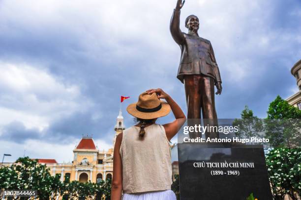 young woman looking at the statue of ho chi minh in ho chi minh city square in vietnam. in the background the city hall building - socialism stock pictures, royalty-free photos & images