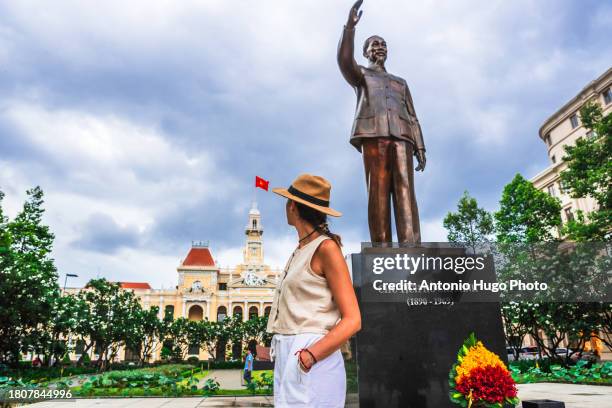 young woman looking at the statue of ho chi minh in ho chi minh city square in vietnam. in the background the city hall building - socialism stock pictures, royalty-free photos & images