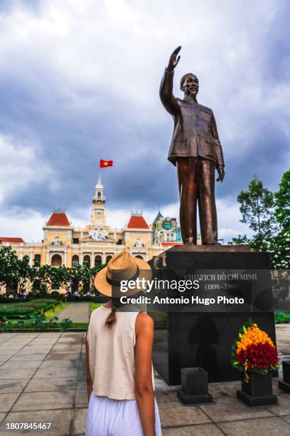 young woman looking at the statue of ho chi minh in ho chi minh city square in vietnam. in the background the city hall building - socialism stock pictures, royalty-free photos & images