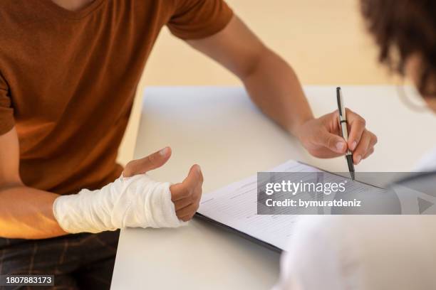 man with broken arm filling health insurance claim form. accident insurance disability compensation - misfortune concept stock pictures, royalty-free photos & images