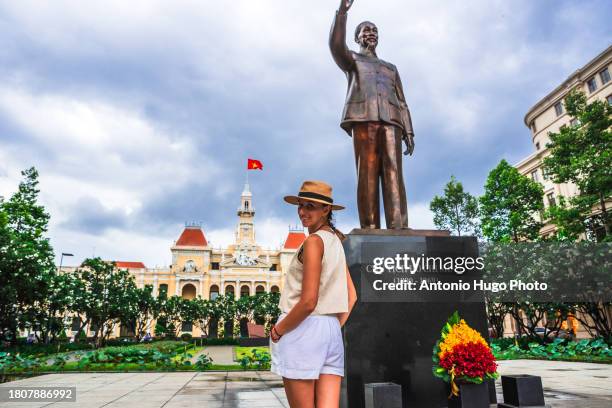 young woman looking at the camera with ho chi minh statue behind her in ho chi minh city square. - socialism stock pictures, royalty-free photos & images