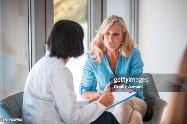 mature caucasian female patient and asian female doctor in doctor's office - mulheres maduras imagens e fotografias de stock