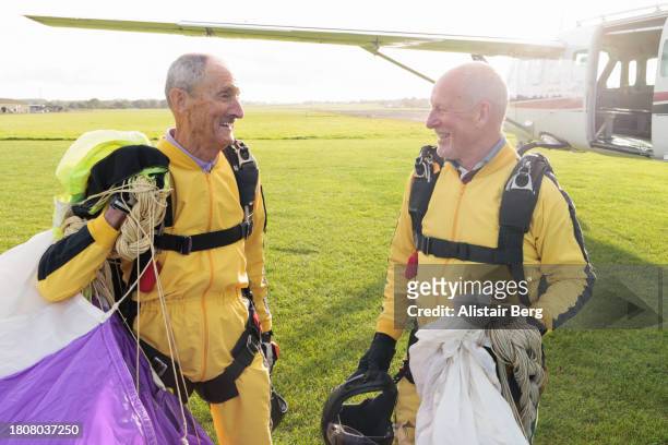 two senior male skydivers after completing a successful parachute jump - afterr stock pictures, royalty-free photos & images
